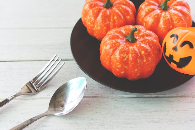 Halloween table setting decoration accessories holiday with pumpkin jack o lantern on black plate and spoon fork on white wood table halloween dinner