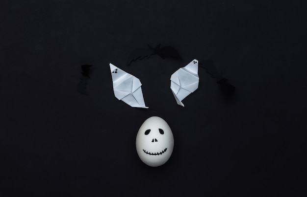 Halloween theme. Egg with hand drawn scary ghost face and ghost on black background