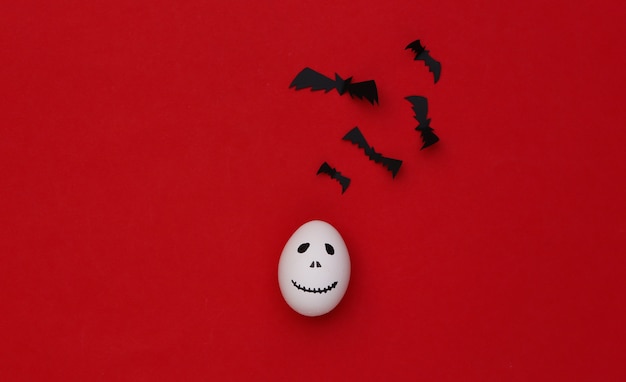 Photo halloween theme. eggs with hand drawn scary ghost face and bats on red background