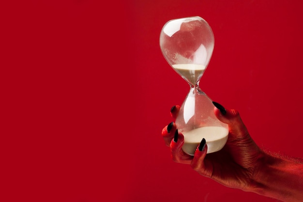 Photo halloween time devil hand holding hourglass timer