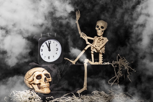 Halloween time a skeleton crawling out of a tomb a skull a\
clock on a black smoky dusty background