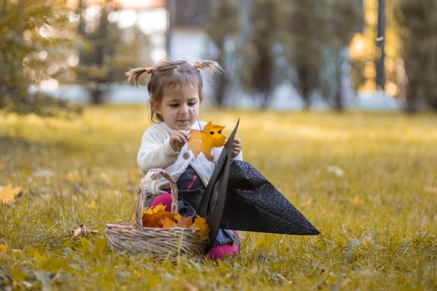 halloween viering concept. schattig klein meisje legt herfstbladeren in heksenhoed in herfstpark.