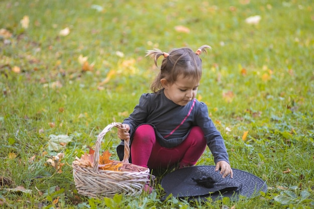 Halloween viering schattig peuter meisje in zwarte jurk spelen met heks hoed op groen gazon met