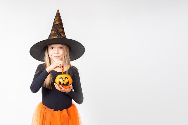 Halloween voor kinderen Een mooi schattig meisje in een heksenkostuum dat een hoed draagt, haalt snoep uit een mand