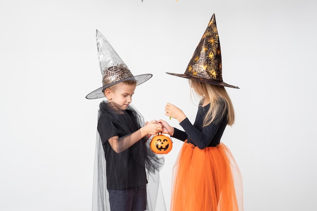 Halloween voor kinderen een mooi schattig meisje in een heksenkostuum en een jongen in een tovenaarskostuum halen snoep uit een mand