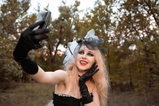 Halloween. A witch in a black suit and red lips takes a selfie