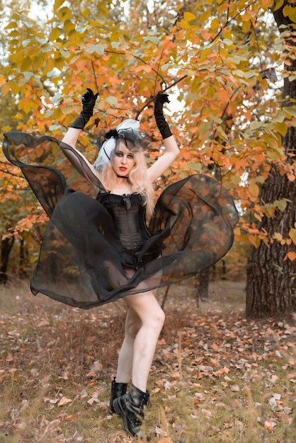 Halloween. A witch in a black suit and red lips throws up a dress in the autumn forest