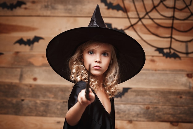 Halloween witch concept - kleine heks kind genieten van spelen met toverstaf. over vleermuis en spinnenweb achtergrond.