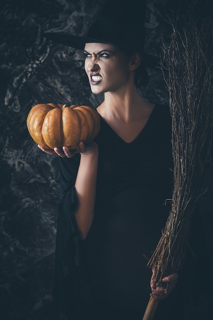 Фото Ведьма хэллоуина держит тыкву и метлу