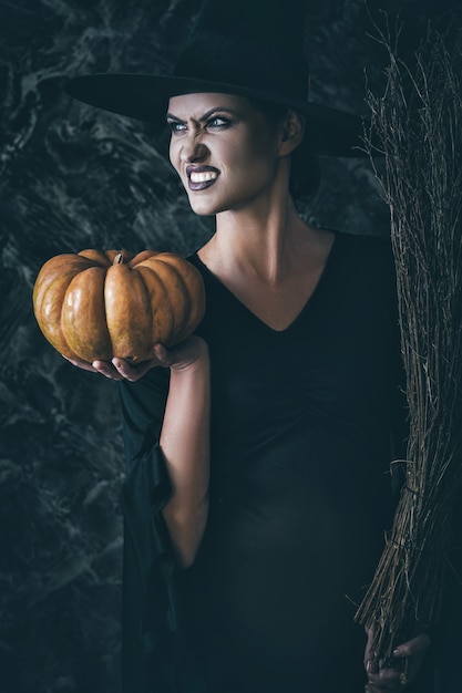 Ведьма Хэллоуина держит тыкву и метлу