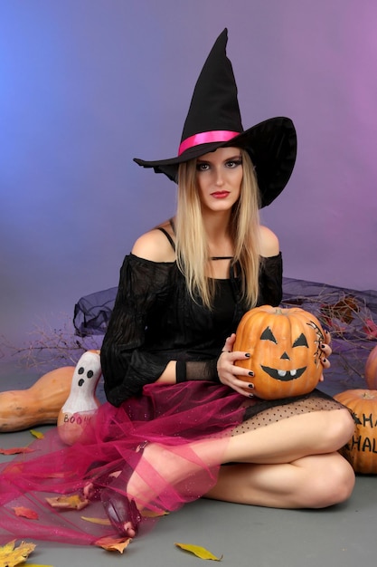 Halloween witch holding pumpkin on color background