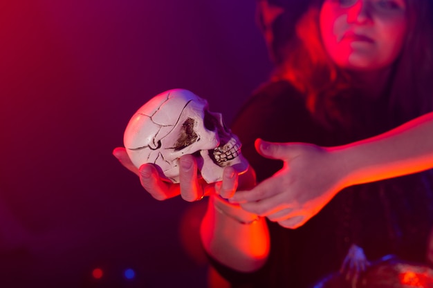 Photo halloween witch making magic with scull in halloween night. magic, holidays and mystic concept.