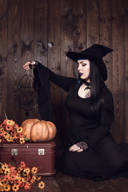 Фото Хэллоуин ведьмы с волшебной тыквой. красивая молодая женщина в шляпе ведьмы и костюме держит резные тыквы джек фонарь. хэллоуин арт дизайн