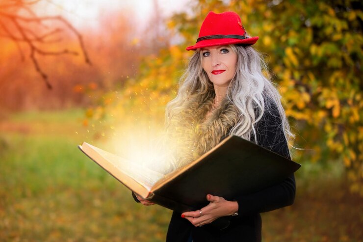 Фотография на хэллоуин женщина с книгой волшебных заклинаний в шляпе ведьмы заклинает, совершая колдовство.