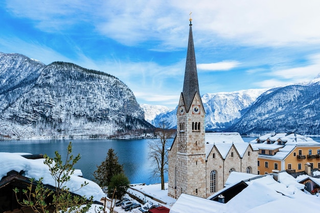 유럽 오스트리아 잘츠부르크 인근 할슈타트. 잘츠카머구트의 겨울. 크리스마스에 호수가 있는 오스트리아 도시로 여행하세요. 눈이 내리는 고산지대. 아름 다운 교회와 알프스 산 근처 마을에 보기.