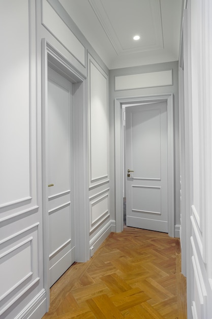 A hallway with white walls and a wooden door that has a black handle and a gold plated plate.