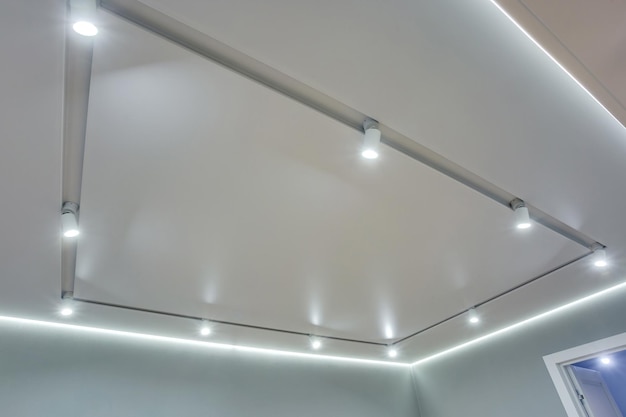 Halogen spots lamps on suspended ceiling and drywall\
construction in in empty room in apartment or house stretch ceiling\
white and complex shape