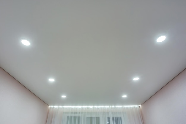 할로겐은 아파트나 집의 빈 방에 있는 매달린 천장과 건식 벽체에 램프를 반점합니다. 스트레치 천장 흰색과 복잡한 모양