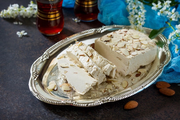 Foto halva met amandelblaadjes en thee op de keukentafel. turkse en arabische zoetigheden. ramadan eten.