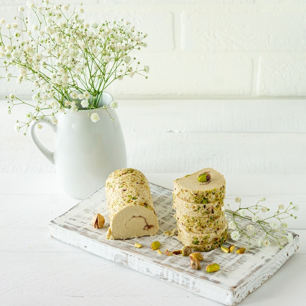 Halva met pistache geserveerd op wit houten bureau met bloemen.