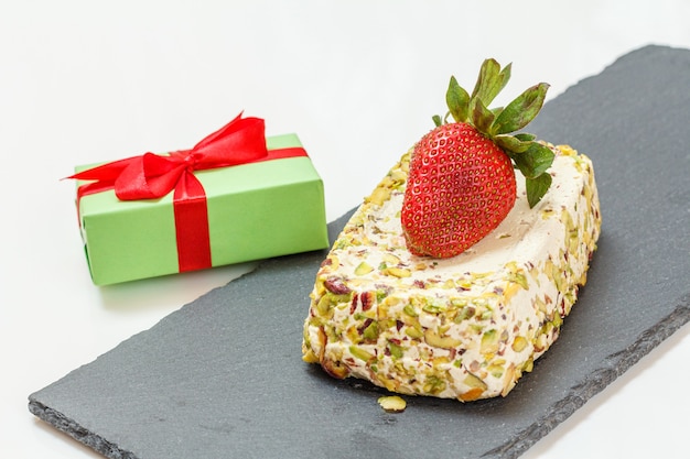 Halva met pistachenoten, een aardbei en een geschenkdoos op een stenen snijplank.