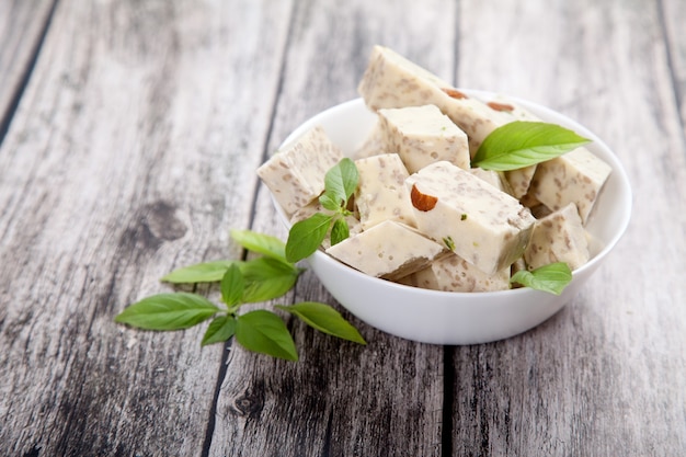 Halva met pistachenoten en amandelen en groene bladeren in een porseleinen kom op een houten ondergrond.