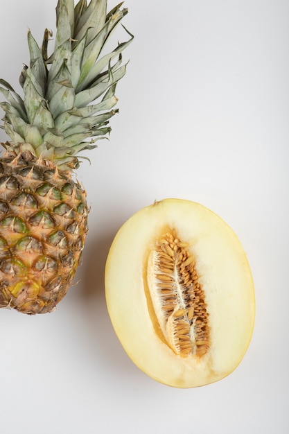 Melone diviso in due e delizioso ananas maturo sul tavolo bianco.