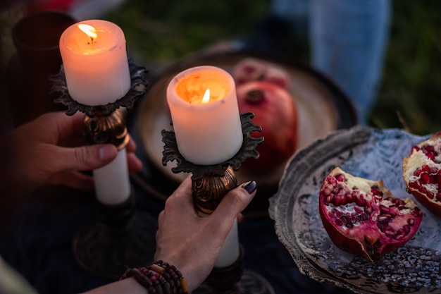 Halved pomegranate on a beautiful plate and hands holding a burning candles