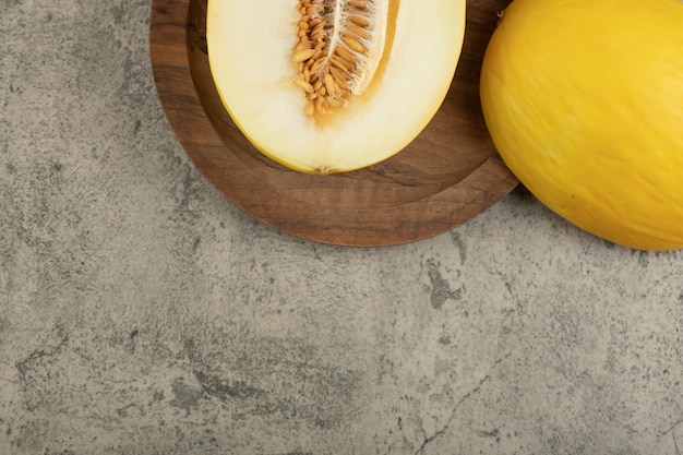 Melone giallo diviso in due e intero delizioso sul piatto di legno.