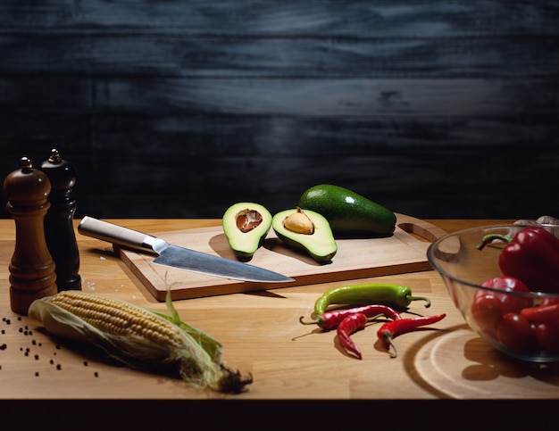 Halved and whole ripe avocados on wooden board with knife