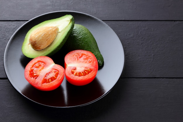 Halves of avocado and tomatoes on black background.