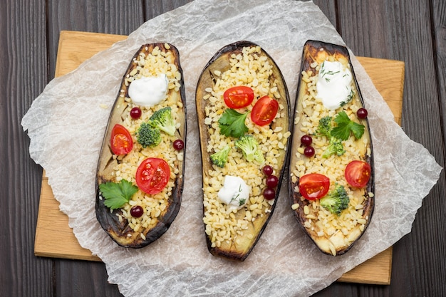 Halves of baked eggplant with bulgur and tomatoes on cutting board