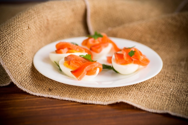 halves of boiled eggs with pieces of salted salmon on a wooden table