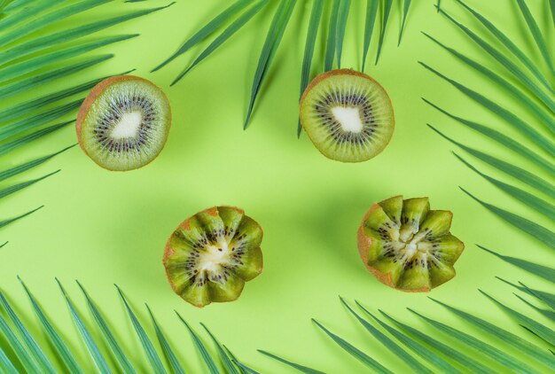 Metà del kiwi verde fresco su uno sfondo verde con foglie tropicali, stendere la frutta colorata