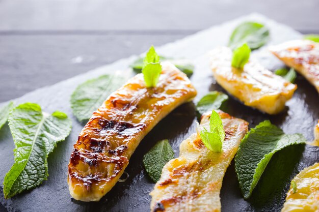 Photo halves of grilled bananas on dark slate board baked banana dessert with mint on dark background