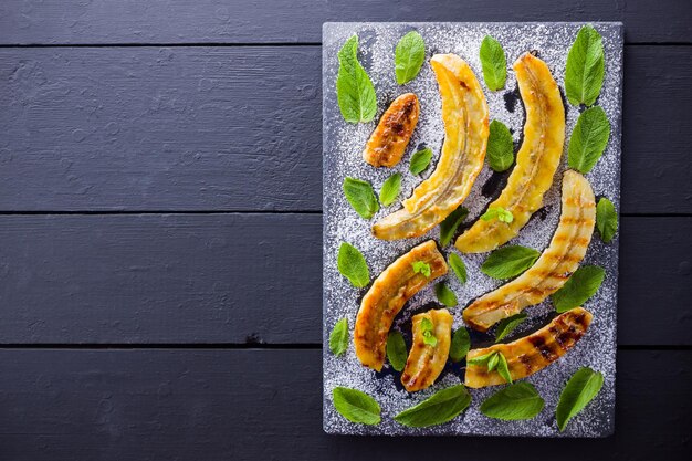 Photo halves of grilled bananas with powdered sugar on slate board baked banana dessert with mint