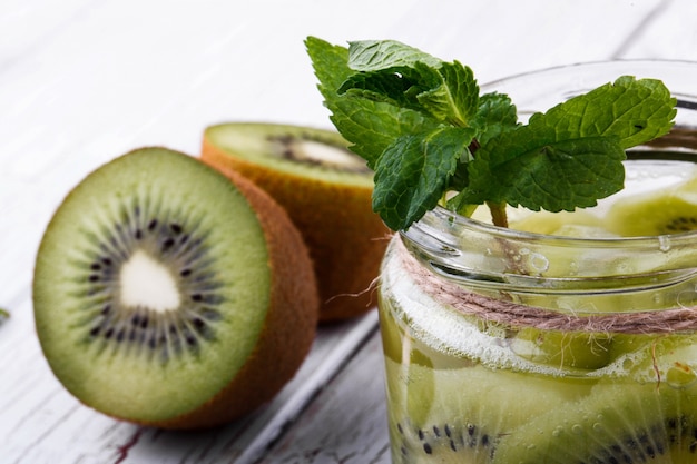 Halves of juicy kiwi lie around bottle with kiwi slices and mint leaves