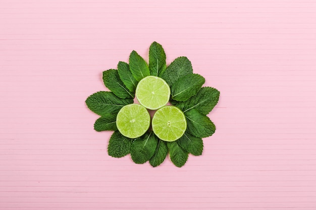 Halves lime and mint on pink wooden background, copy space