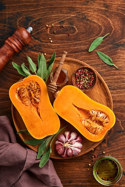 Halves of raw organic butternut squash with sage leaf, multicolored pepper garlic, honey, salt and pepper on old wooden background. Food background. Top view with copy space.