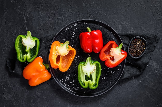 Halves of sliced orange, green and red bell peppers. Black background. Top view