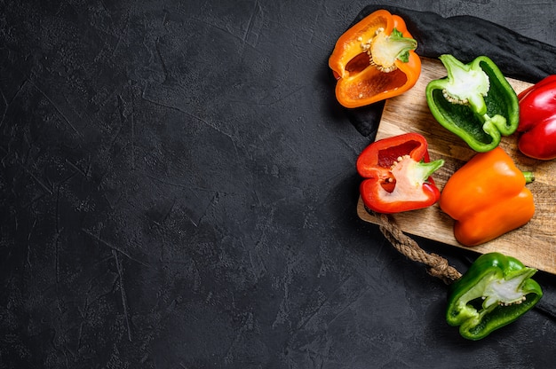 Halves of sliced orange, green and red sweet peppers. Black background. Top view. Space for text