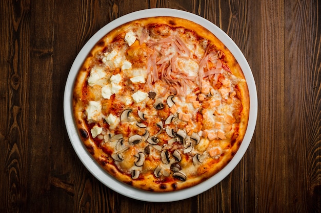 Ham, fish, mushroom and feta cheese pizza, wooden background, low key, top view