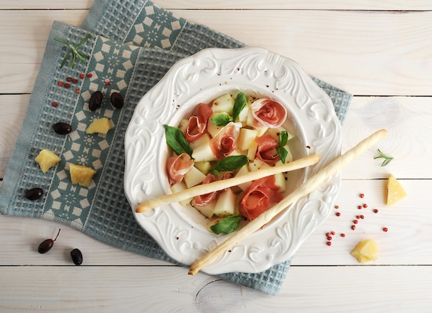 Ham met meloen en soepstengels op een plaat, olijven en Parmezaanse kaas