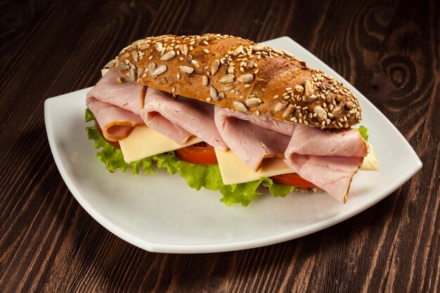 Ham sandwich with lettuce cheese tomato on plate on wooden table