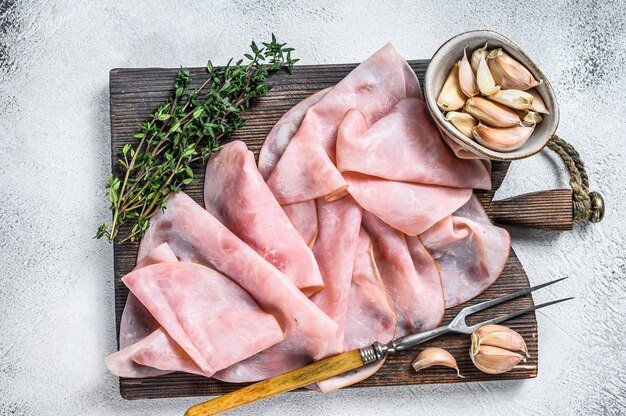 Ham Thin sliced on wooden cutting board with herbs. White background. Top view.