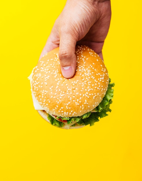 Foto hamburger die over gele achtergrond wordt gehouden