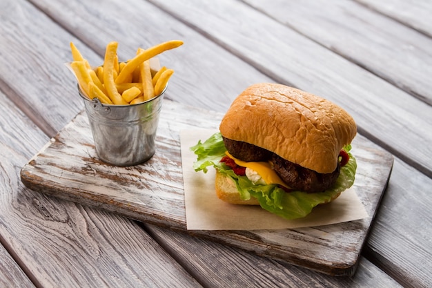 Hamburger en emmer frietjes. Hamburger op stuk papier. Heerlijke fastfoodmaaltijd. Traditioneel recept van beefburger.