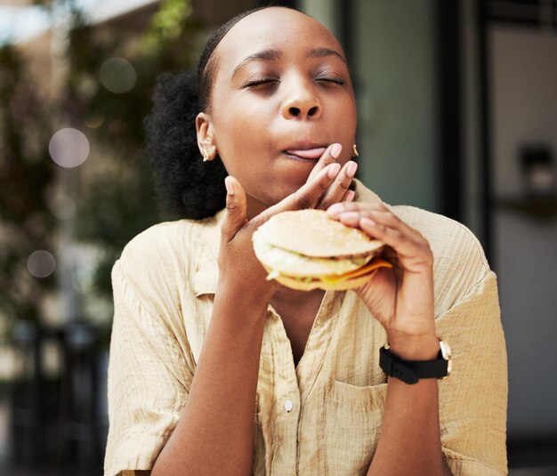 Photo hamburger fast food and black woman eating a brunch in an outdoor restaurant as a lunch meal craving deal breakfast sandwich and young female person or customer enjoying a tasty unhealthy snack