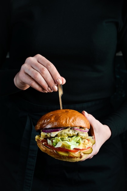 Hamburger in de handen van de chef-kok fastfood concept op een donkere achtergrond