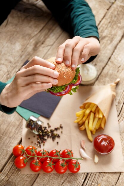 Hamburger in handen frietjes sauzen kruiden op een houten achtergrond Fast food concept